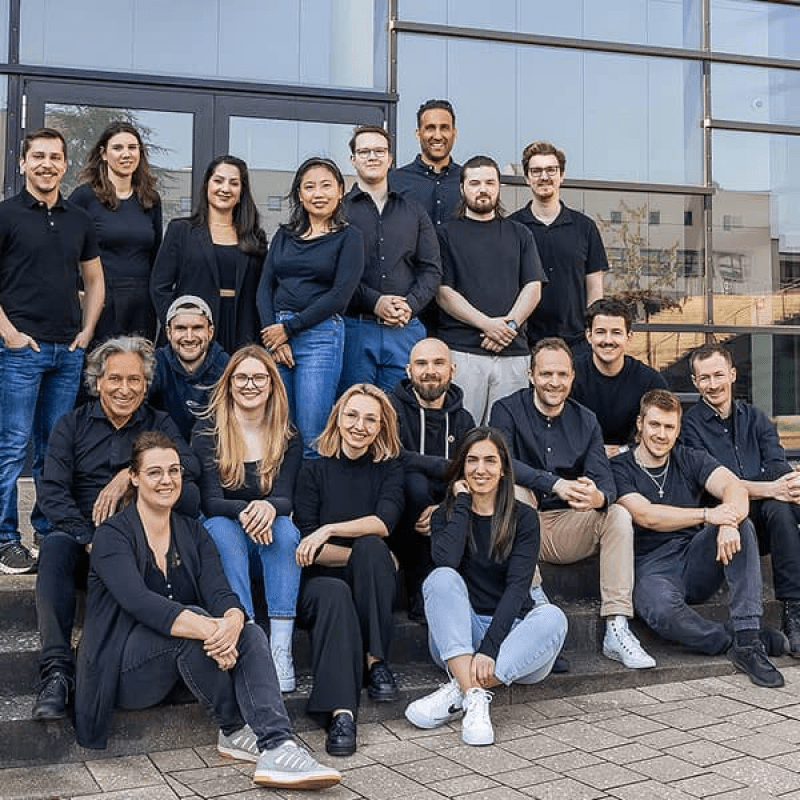 Gruppenfoto des mindtwo Teams auf einer Au&szlig;entreppe, alle in schwarzer Kleidung, l&auml;chelnd in die Kamera