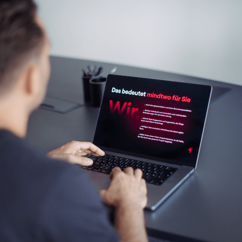 Person betrachtet einen Laptop mit einer mindtwo-Folie, auf der Unternehmenswerte angezeigt werden.