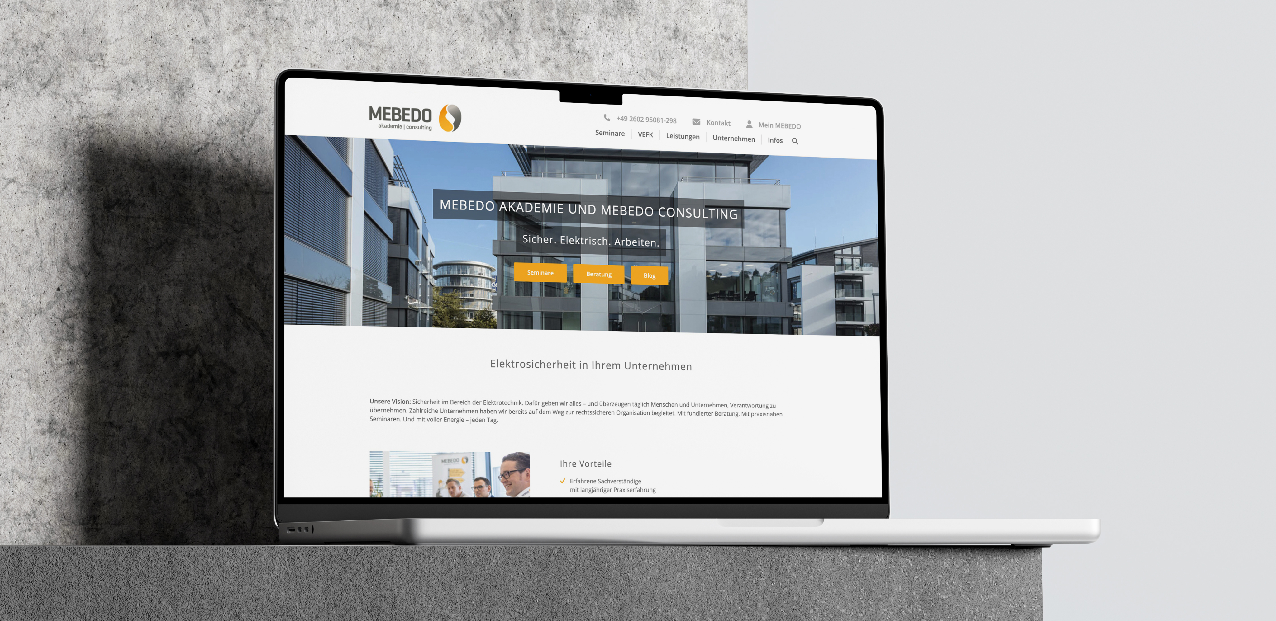 Laptop-Mockup auf Steinsockel zeigt die MEBEDO-Homepage für Akademie und Consulting mit dem Slogan „Sicher. Elektrisch. Arbeiten.“